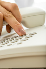 Closeup of female hand dialing a telephone number on a white lan - obrazy, fototapety, plakaty