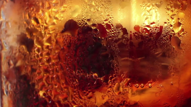 Macro ECU of ice being gently stirred in a glass of cola-colored liquid.

