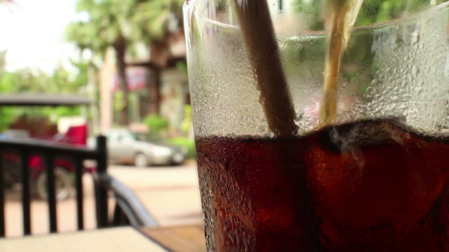 Close up of a glass of cola-colored fizzy drink with straw stirring ice and d
