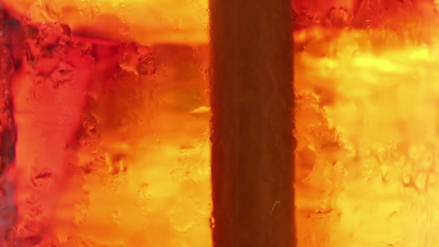 Macro extreme close up of ice being stirred in a cola-colored fizzy drink; a
