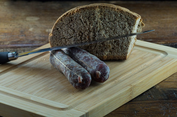 Pane nero e salamino, salame affettato su tagliere con pane scuro, coltello per salumi