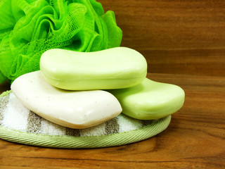 white and green soap with plastic bath puff on wooden background
