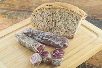 Pane nero e salamino, salame affettato su tagliere con pane scuro, coltello per salumi