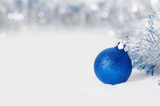 Blue Christmas ball with garland. Bokeh effect on white background. Copyspace for your greeting or wishes