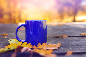 Blue cup on wooden table with autumn blurred background