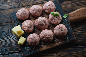 Raw meatballs with seasonings on a rustic wooden cutting board