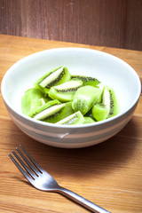 Bowl of delicious chopped kiwi only salad  in a rustic kitchen , on a wooden table with a metal fork  in the frame