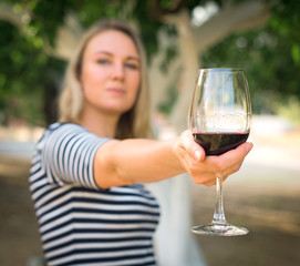 Woman offering glass of red wine outdoors.