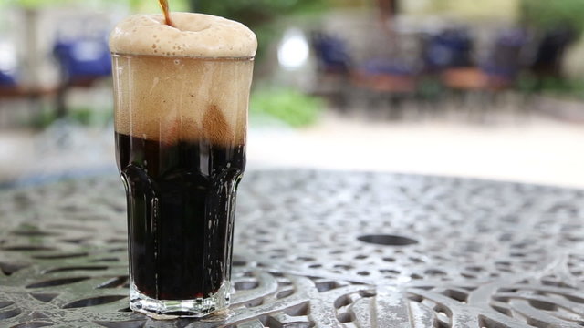 A full glass of frothy dark beer standing on a table and flowing through the top