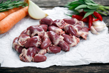 Raw Duck hearts on crumpled paper, decorated with greens and vegetables. on old wooden table