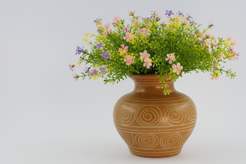 Colorful artificial flower and green leaf in a brown vase