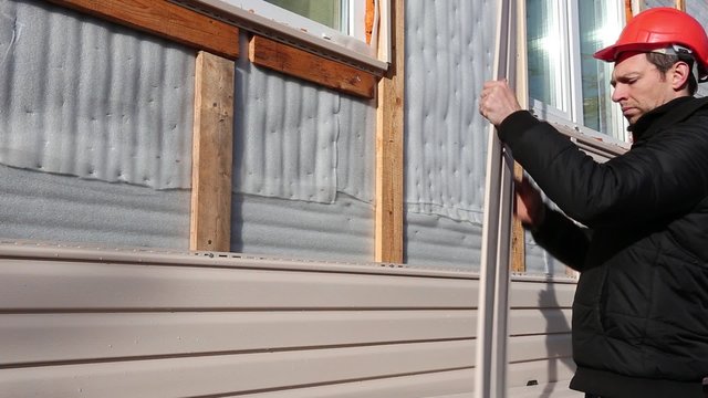 A worker installs panels beige siding on the facade of the house