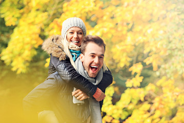 Young romantic couple piggybacking in the park in autumn