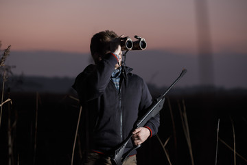 Hunter man with rifle see in binocular in field in evening