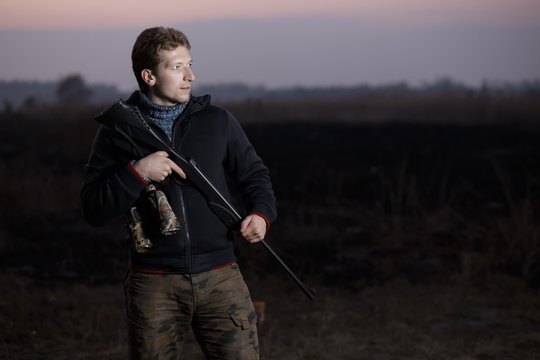 Huntsman with rifle standing on guard in field in evening