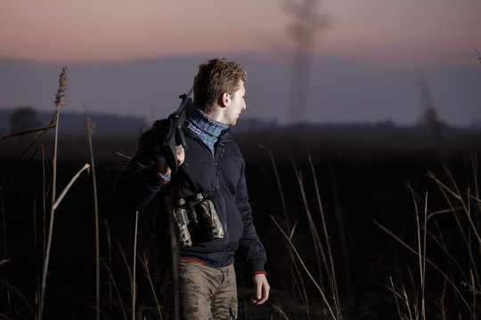 Man hunter with gun standing on guard in field in evening