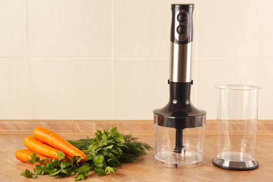 Fresh carrots with herbs and a blender on the kitchen table