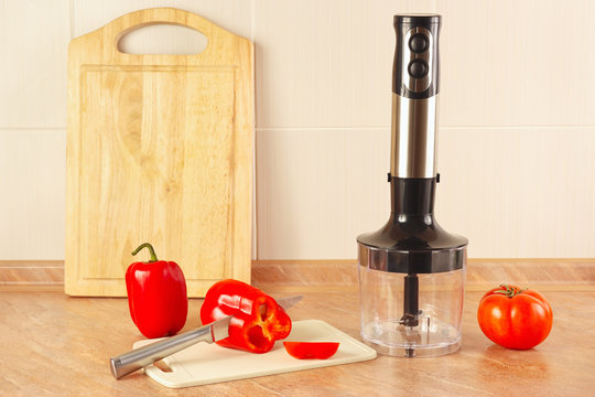 Chopped red bellpepper with tomato and a blender on the kitchen table