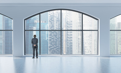 Rear view of a person in formal suit who is looking out the window in a modern clean interior with huge panoramic windows. Singapore city view.