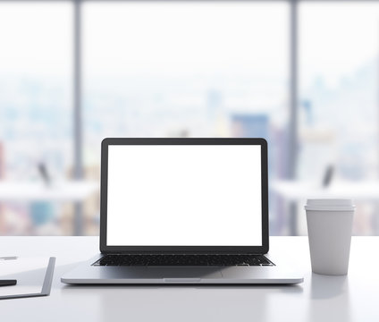 There are a laptop with white copy space screen, legal pad and a cup of coffee on the table. 3D rendering. Modern office with panoramic New York view in blur on the background.