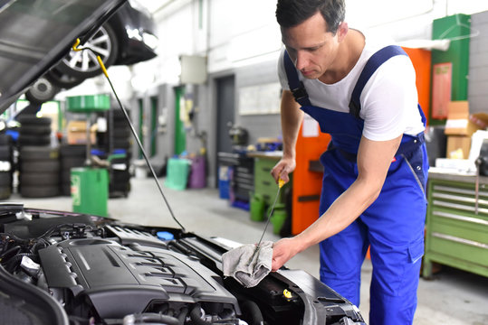 Mechaniker in einer Werkstatt kontrolliert den Füllstand vom Motoröl eines Autos // mechanic in a workshop controls the level of the oil of a car