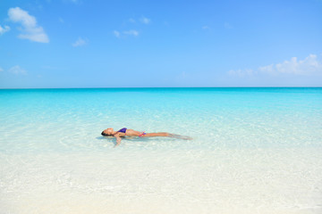 Fototapeta na wymiar Woman swimming in ocean relaxing enjoying the sun bathing in peaceful blue water. Sexy female adult floating meditating in the sea.