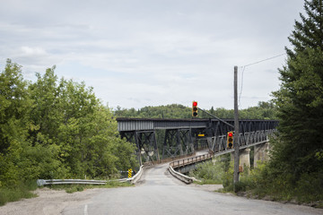 horizontal image of a highway leading up to a huge black structural iron bridge with a stop light  surrounded by green trees in the summer time.