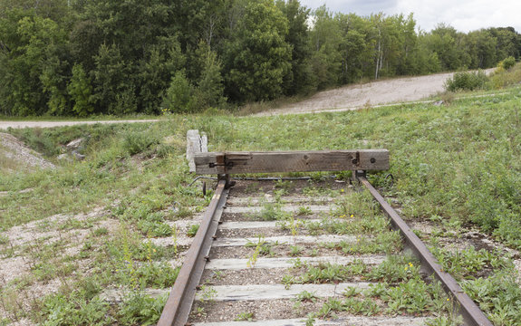 horizontal image of the end of a railroad track going no where with green grass all around.