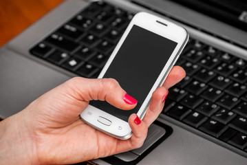 Woman's hand with a smartphone on the background notebook