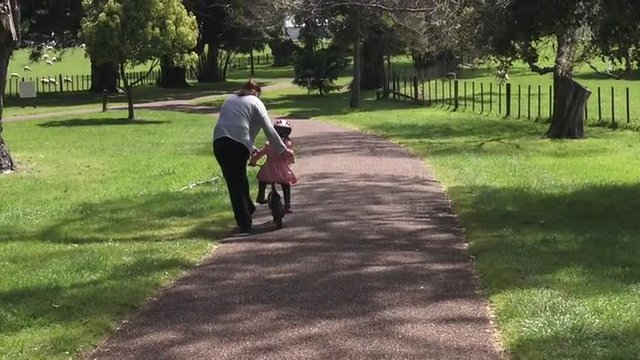 Parent (Young mother age 30) teaching a child (girl age 5-6) how to ride bicycle without stabilizers in the park