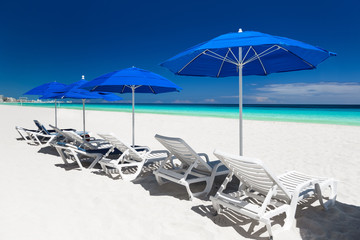 Caribbean beach with blue sun umbrellas and white beds