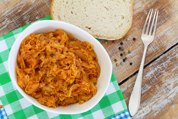 Polish bigos in white bowl on rustic wooden surface

