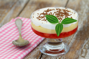 Traditional English strawberry trifle in transparent dessert glass on rustic wooden surface

