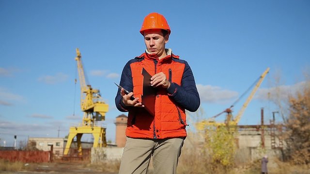 man construction worker in an orange helmet holding documents background blue sky and crane