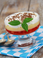 Strawberry trifle in dessert glass on checkered cloth on rustic wooden surface

