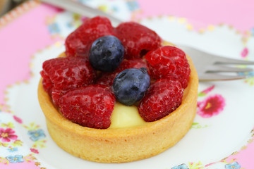 Delicious crunchy tartelette with custard, fresh raspberries and blueberries, closeup
