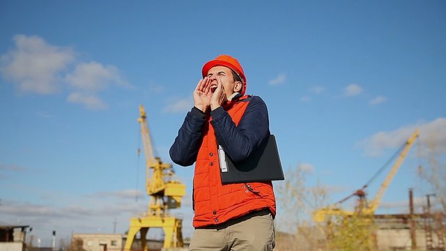 builder man in a helmet corrects orange shouts calling shout against the blue sky and a crane