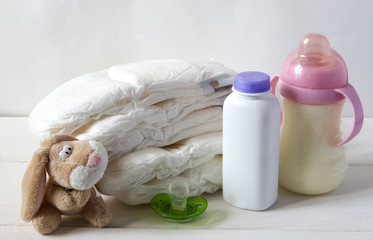 New born child stack of diapers, nipple soother, bunny toy and baby feeding bottle with milk on a...