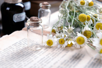 Old book with dry flowers and bottles on table close up