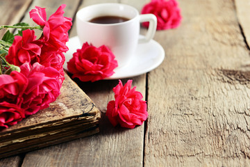 Fototapeta na wymiar Old book with beautiful roses and cup of coffee on wooden table close up