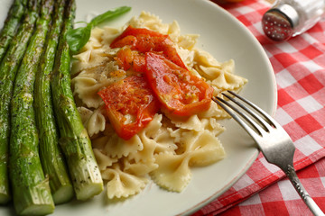 Roasted asparagus and tasty pasta with vegetables on plate on wooden table background