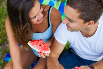 Couple sitting on a picnic blanket and eating watermelon.