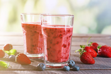 Glasses of berry smoothie on wooden table on blurred background