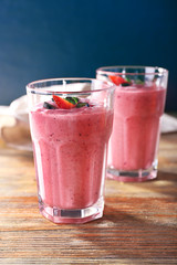 Glasses of berry smoothie on wooden table on dark background