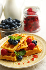 Sweet homemade waffles with forest berries and sauce on table background