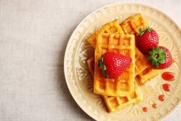 Sweet homemade waffles with fresh strawberries on plate, on light background