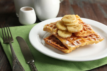 Sweet homemade waffles with sliced banana on plate, on light background