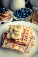 Sweet homemade waffles with sliced banana on plate, on light background