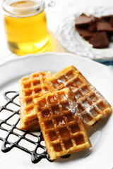 Sweet homemade waffles with chocolate sauce on plate, on light background