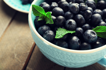 Fresh blueberries in cup on wooden table close up